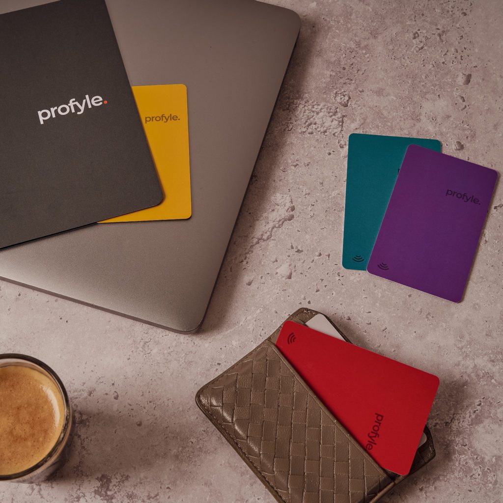 Profyle cards in various colors on a laptop, next to a wallet and coffee cup.