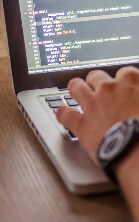 Close-up of a hand typing on a laptop keyboard with code displayed on the screen