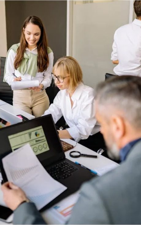 Three people working in an office: a man reviewing documents, a woman on a laptop, and another woman writing.