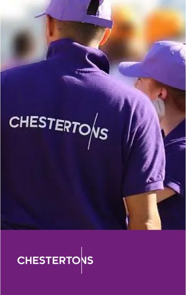Back of person in purple polo shirt with 'CHESTERTONS' logo and purple cap. Another person in a purple cap is partially