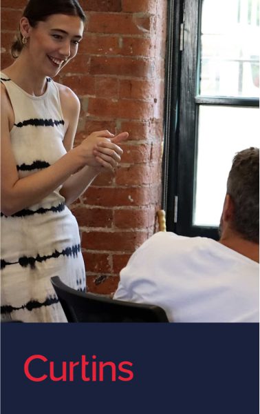 Woman in tie-dye dress talking to a man, with 'Curtins' text on a blue banner