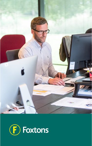Man in glasses working at a desk with computers. Foxtons logo at the bottom.