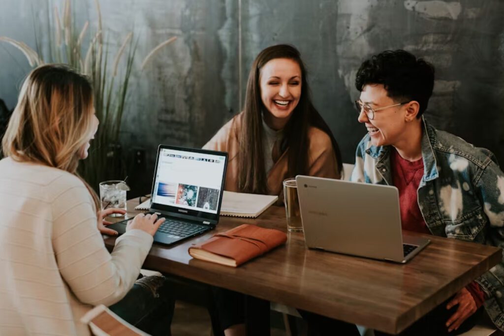 Three people laughing and working on laptops at a table.