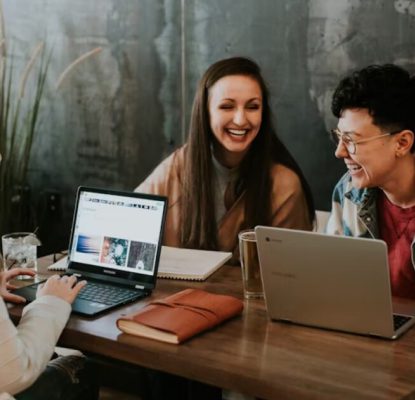 Three people laughing and working on laptops at a table.