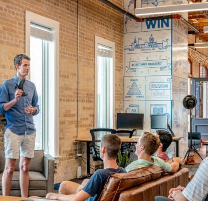 Man presenting to a group of people in a modern office with brick walls and wall graphics.