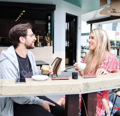 Man and woman smiling and talking at an outdoor cafe table with drinks.