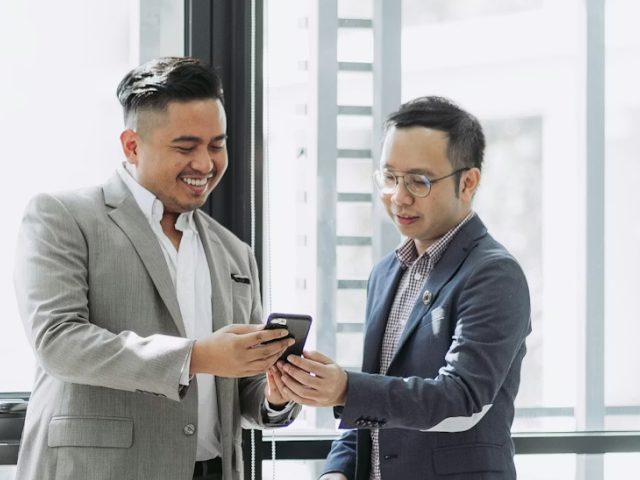Two men in suits smiling while looking at a smartphone