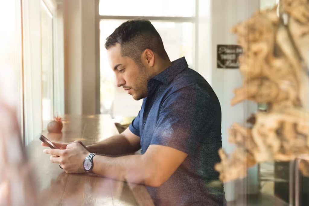 Man in a blue shirt looking at his smartphone at a wooden counter.